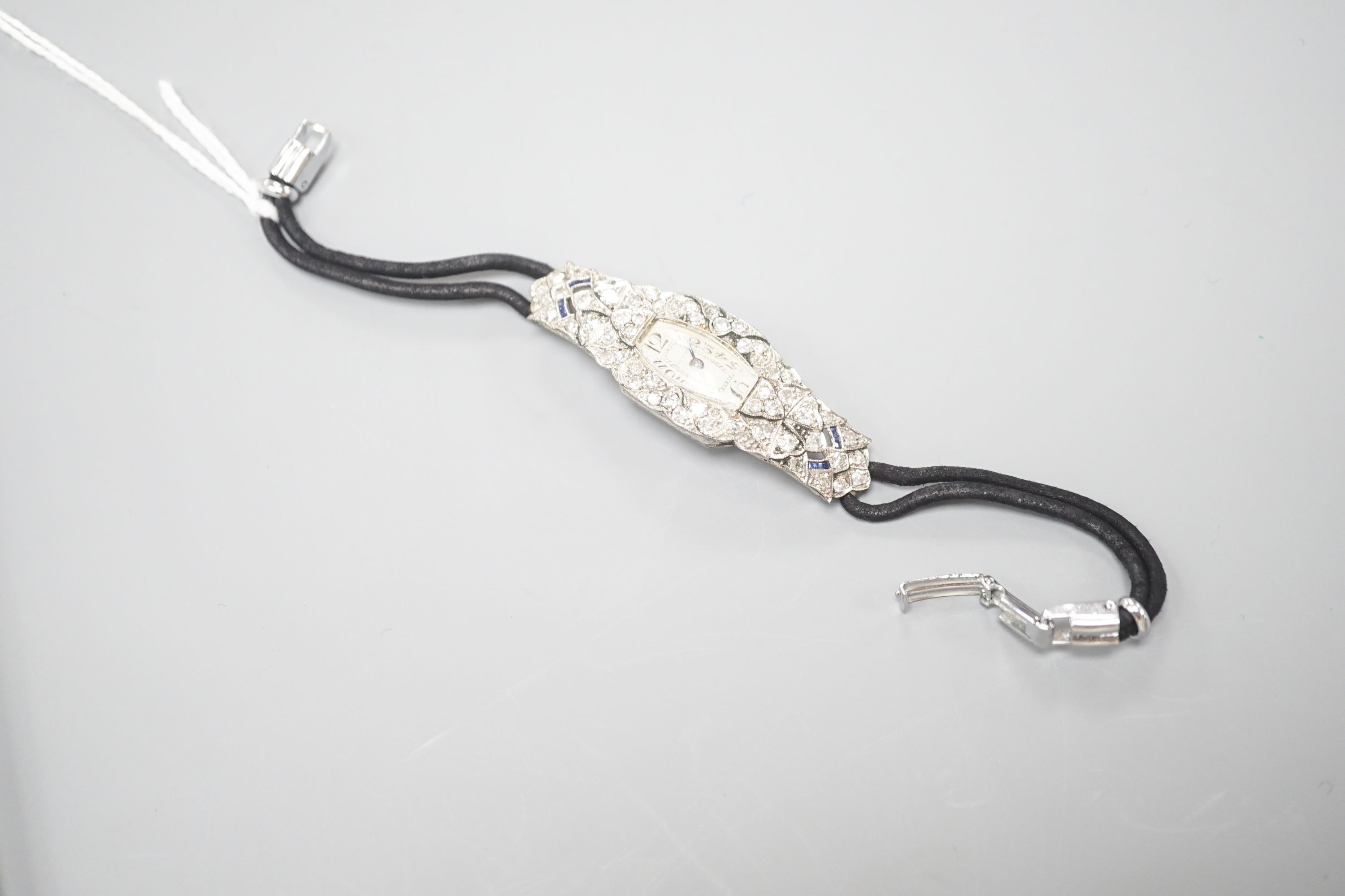 A lady's mid 20th century engraved white metal, diamond and sapphire set cocktail watch, case diameter 17mm, gross weight 18.3 grams, on a later? twin strand fabric strap.